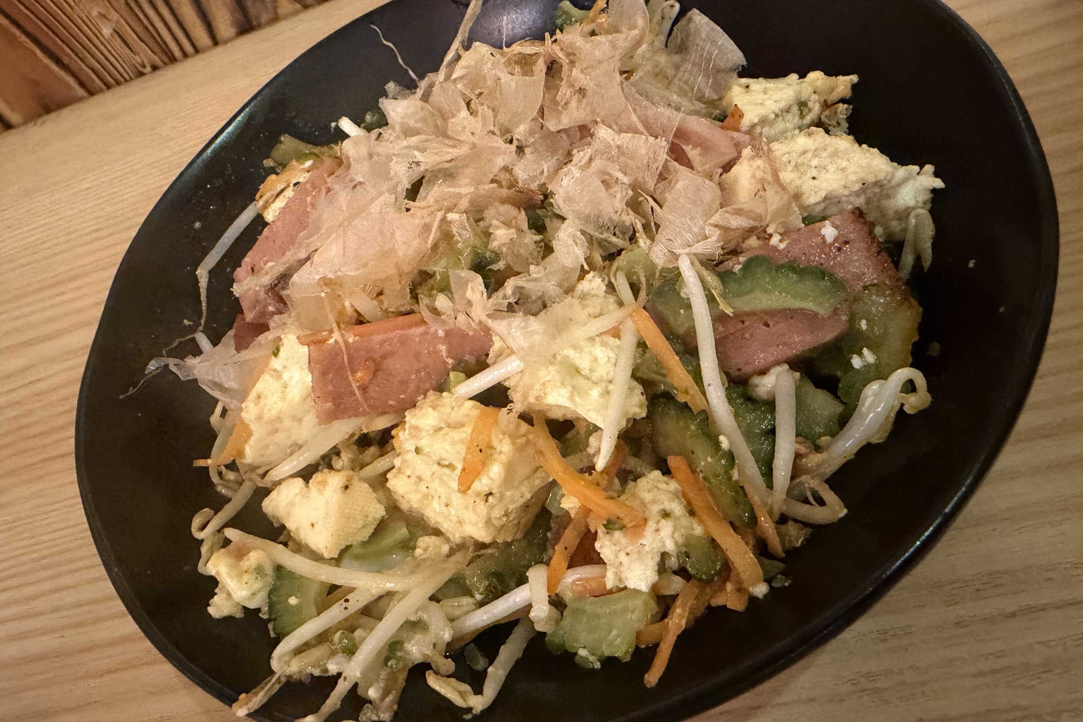 ゴーヤチャンプルーの写真。ゴーヤ、豆腐、卵、加工した豚肉を炒めた上にかつお節がかかっている。