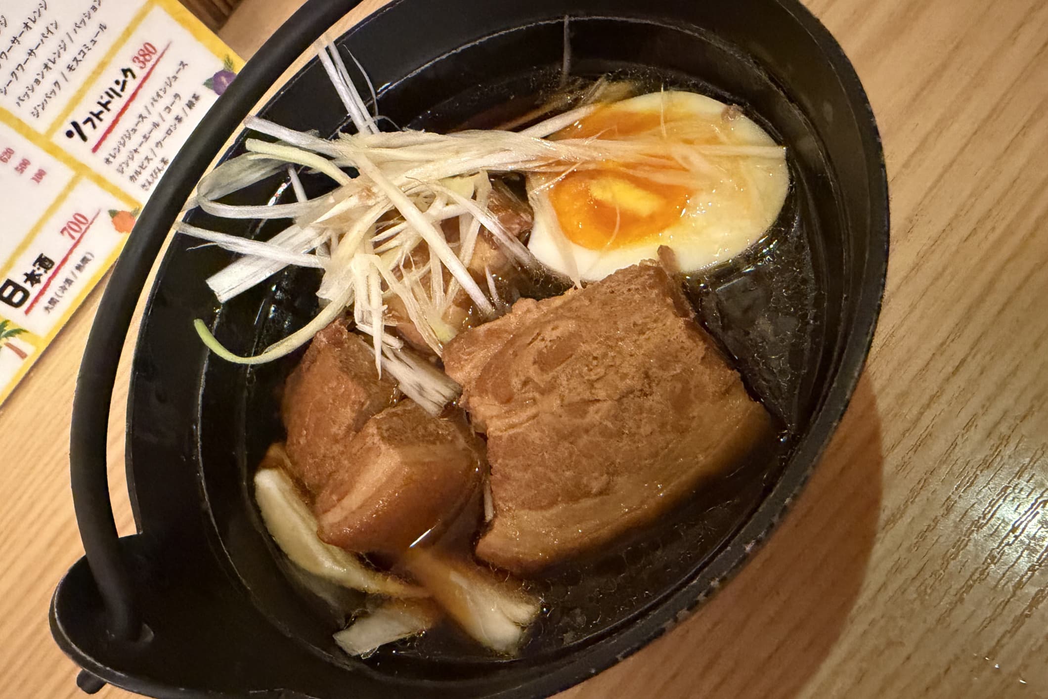 ラフテーの写真。黒い器に煮込んだ角切りの肉と卵とネギが盛り付けられている。