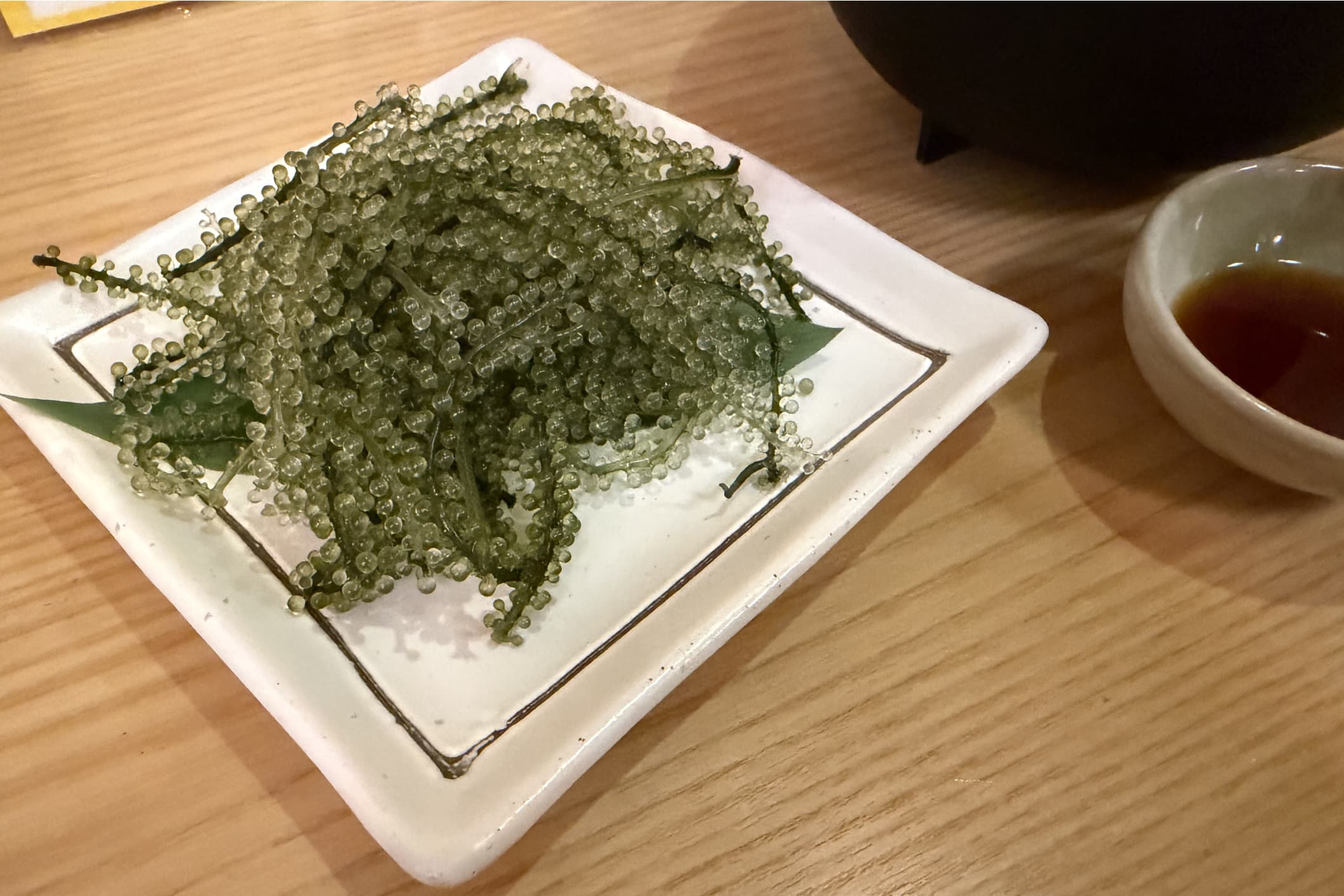 四角の白い皿の上に海ぶどうが盛り付けられており、右にポン酢が入った小皿が置かれている。